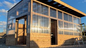 A modern building with large windows and a wooden exterior, surrounded by gravel.