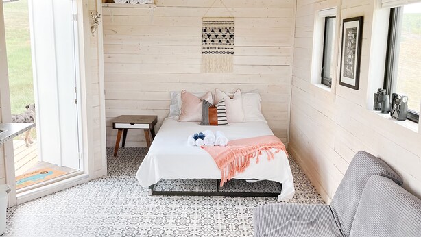 A bedroom with a bed, a bench, a wall-mounted macrame, and a window.