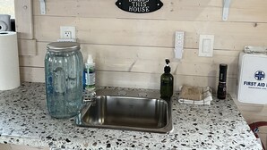 A kitchenette with a stainless steel sink, a coffee maker, and a sign that reads "Bless This House."