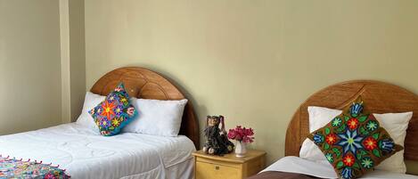 Un dormitorio con dos camas individuales, una mesita de noche con lámpara y un cojín decorativo.