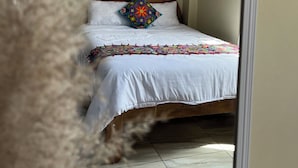 Un dormitorio con una cama, un cojín colorido y una colcha blanca.