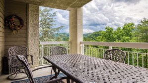 A covered outdoor patio with a table and chairs, a decorative wreath, and a view of green hills.
