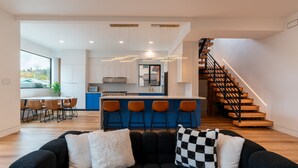 A modern living room with a sofa, a kitchen area with bar stools, and a staircase. - Spacious Modern Escape Near UO Campus (Eugene)