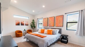 A modern bedroom with a large bed, a desk, and a chair. There are three paintings on the wall and a plant. - Spacious Modern Escape Near UO Campus (Eugene)