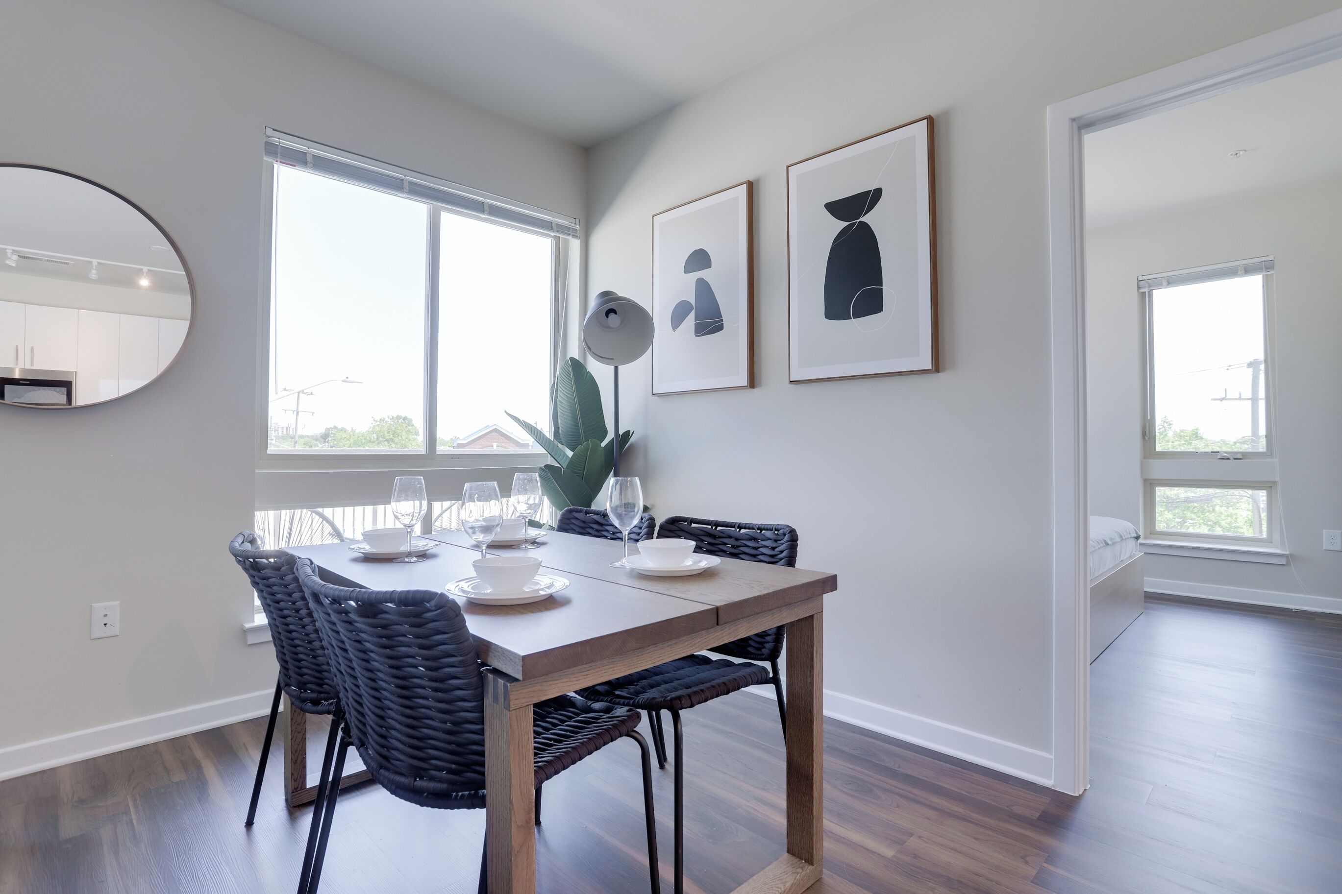 A dining area with a wooden table, dark wicker chairs, and a large window providing natural light.