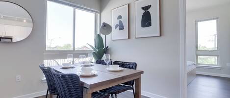 A dining area with a wooden table, dark wicker chairs, and a large window providing natural light.