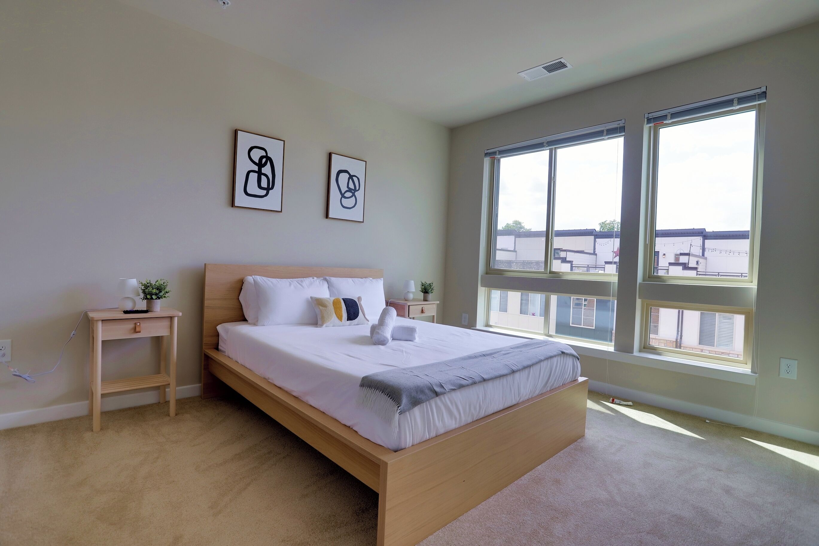 A bedroom with a large bed, two bedside tables, a small plant, and two framed pictures on the wall.