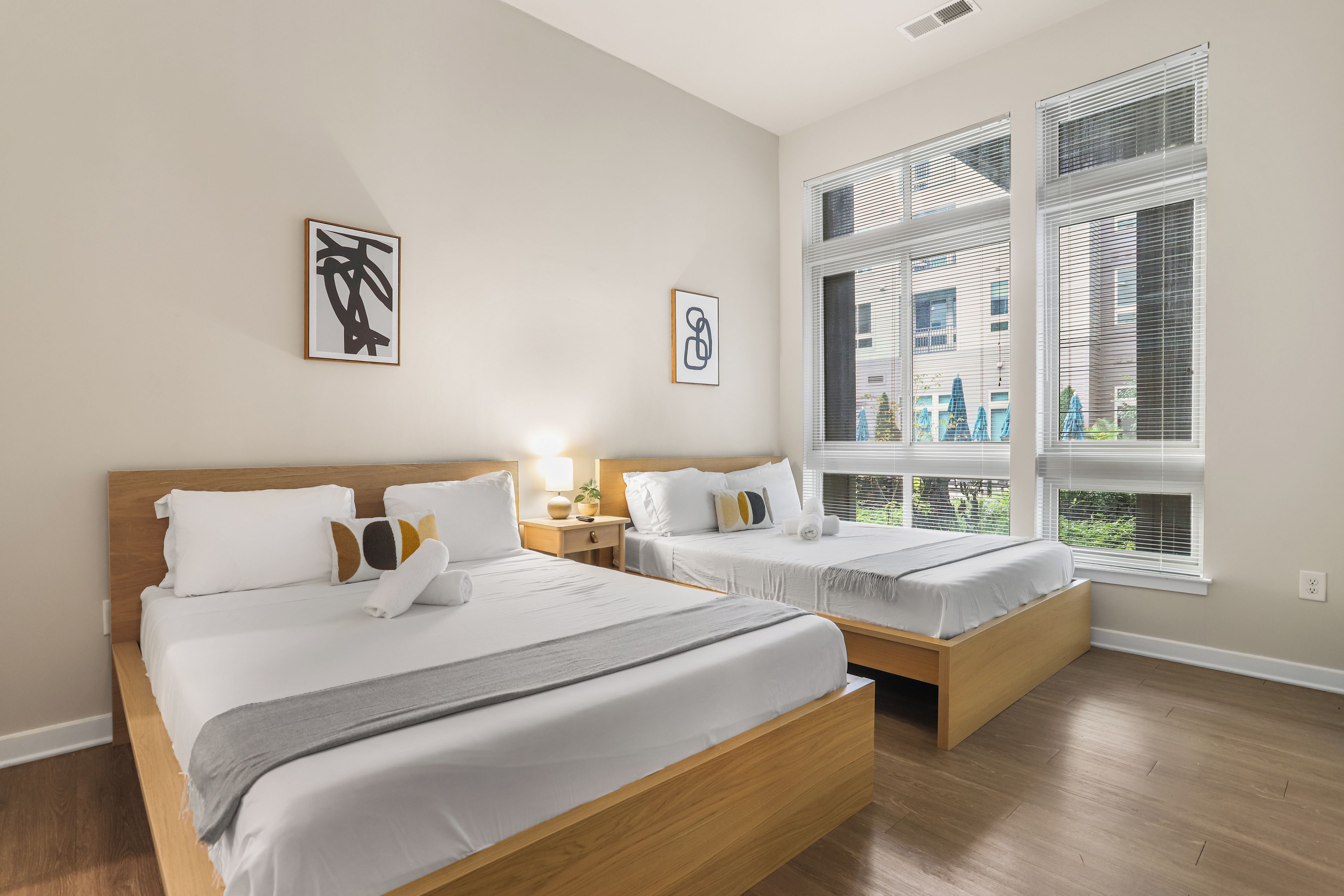Une chambre d’hôtel avec deux lits, une grande fenêtre avec des stores et des œuvres d’art accrochées au mur.