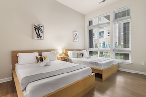 A hotel room with two beds, a large window with blinds, and artwork on the wall. - Huntington Apartments near Cameron Run - We Host (Alexandria)