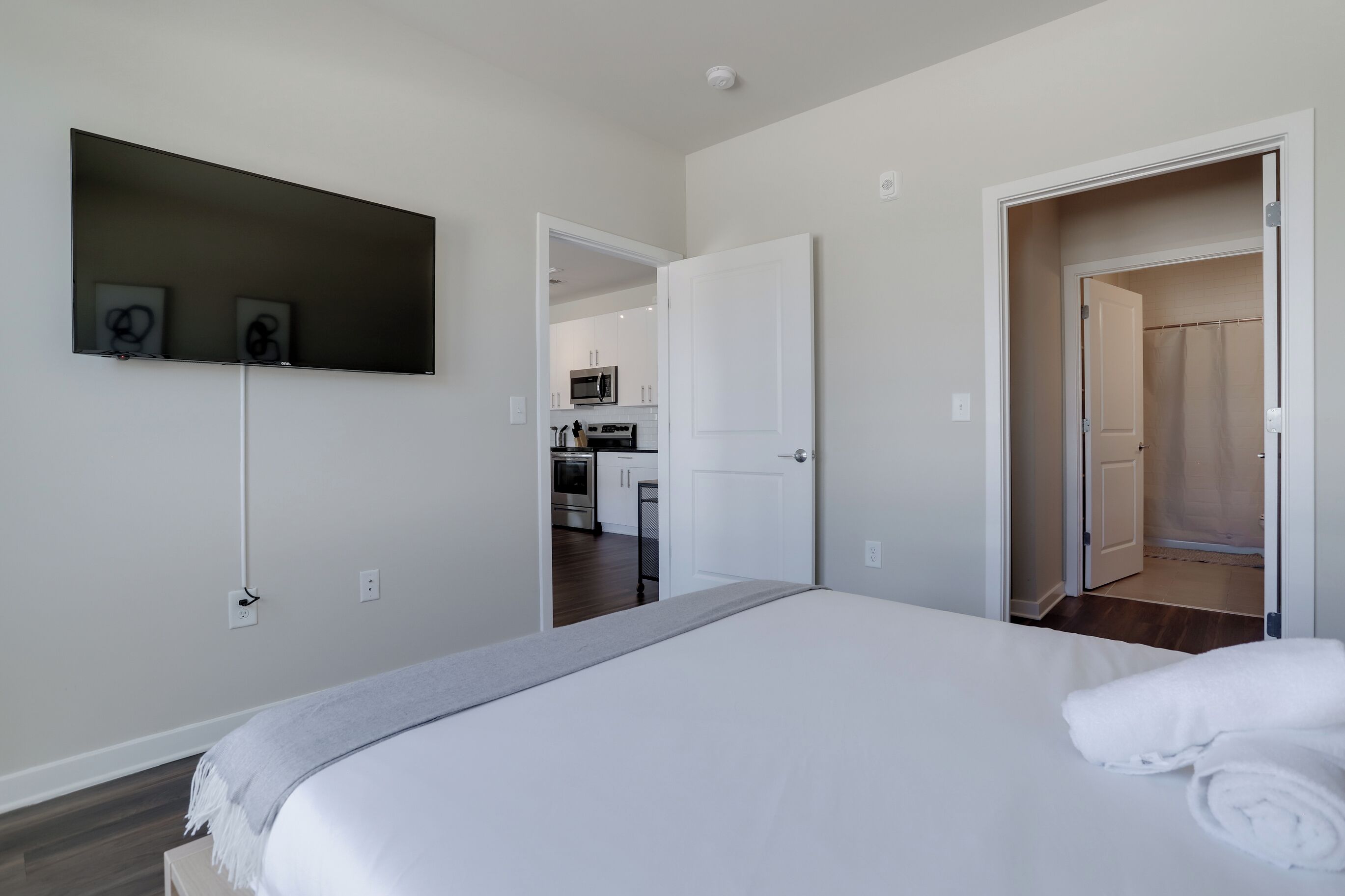 Une chambre avec un lit, un téléviseur à écran plat fixé au mur et une vue sur la cuisine.