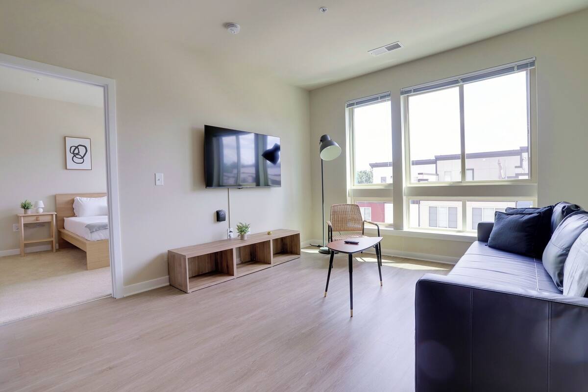A modern living room with a sofa, a TV, a lamp, and a window.