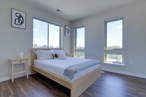 A bedroom with a wooden bed, two bedside tables, and large windows with blinds.