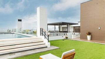 Un espace piscine aménagé sur le toit, offrant une vue dégagée sur les toits de la ville, une cuisine extérieure moderne et une pelouse bien entretenue.