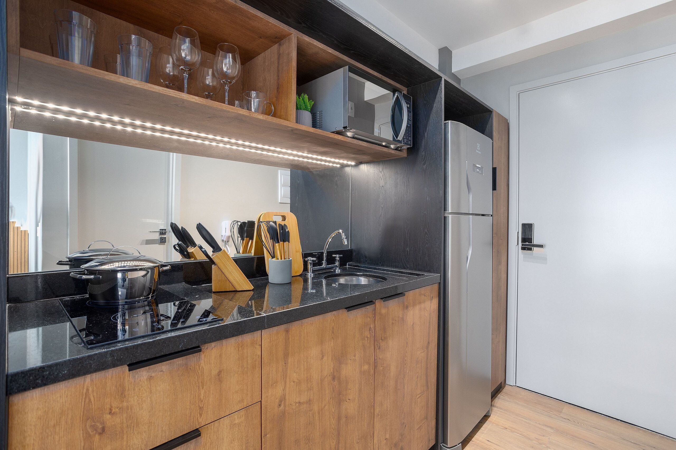A modern kitchen with a black countertop, wooden cabinets, a stainless steel refrigerator, and a built-in microwave.