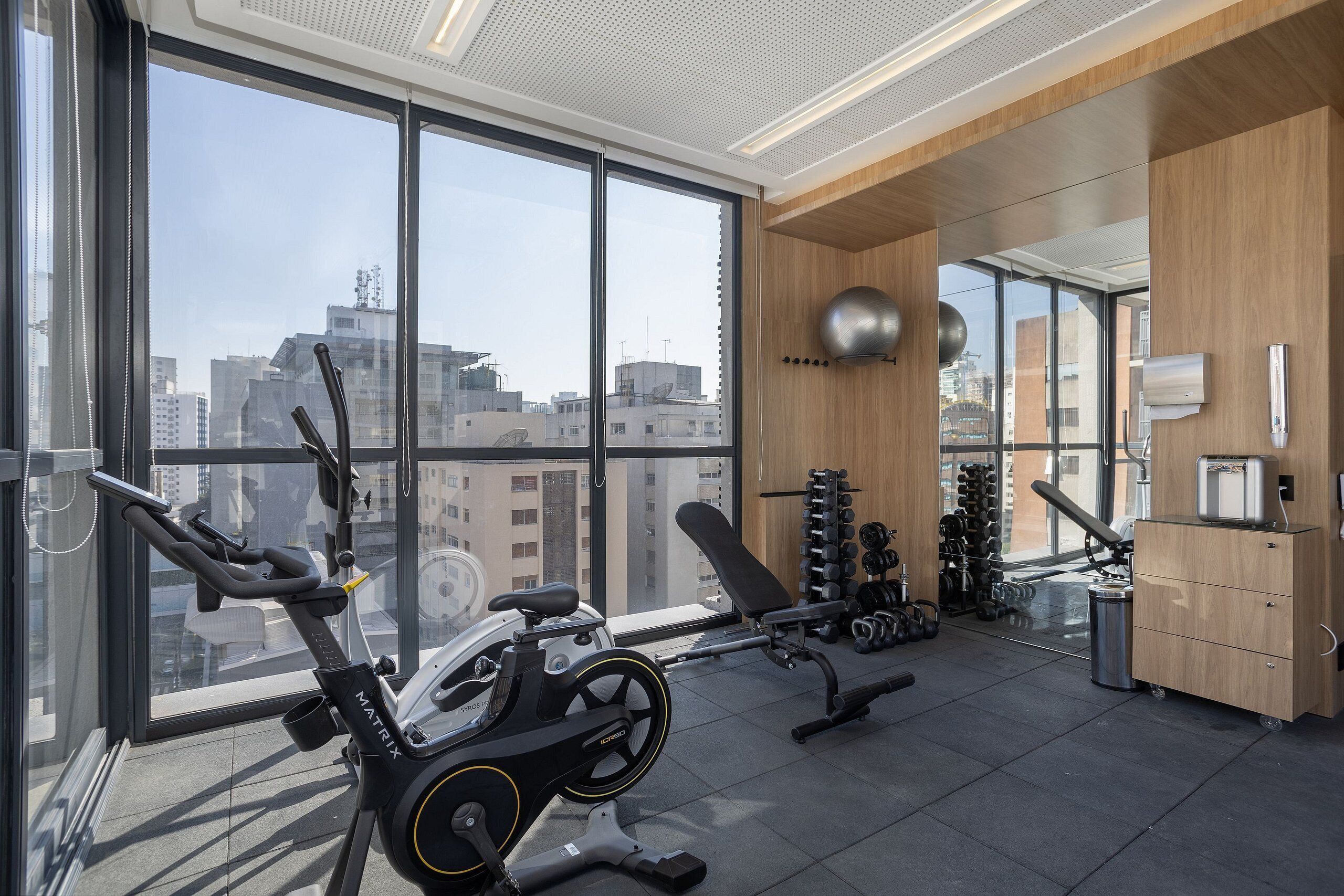 Ein modernes Fitnessstudio mit Trainingsgeräten, großen Fenstern und Blick auf die Stadtlandschaft.