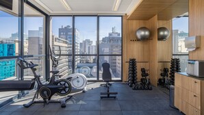 Une salle de sport équipée de matériel d’exercice, dotée de grandes fenêtres et offrant une vue sur la ville.