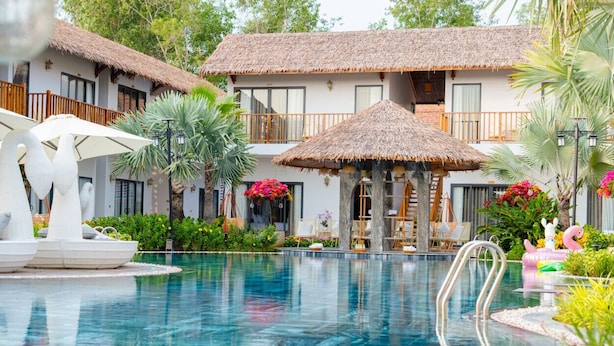 A pool with a thatched roof structure, surrounded by lush greenery and a two-story building with balconies. - Greenlife Village Phu Quoc (Phu Quoc)
