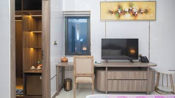 A hotel room with a wooden desk, a television, a small chair, a bedside table, and a bed with a patterned bedspread.