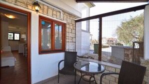 A patio area with two wicker chairs and a small table, a stone wall, and a window overlooking a street. - Greta studio 1 with terrace (Rovinj)