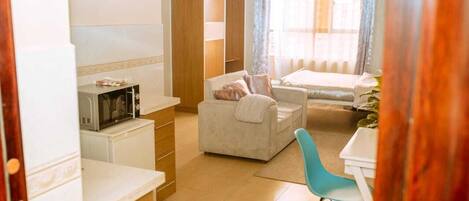 Un espacio habitable compacto con kitchenette, sofá, mesa de comedor y cama.