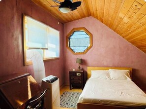 A bedroom with a sloped ceiling, a bed, a nightstand, a heater, and a window with blinds.