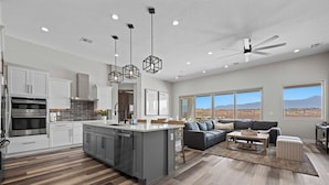 A modern kitchen with a central island, white cabinetry, and a dining area with a sofa and coffee table. - Mountains and Saltwater Pool (Mesquite)