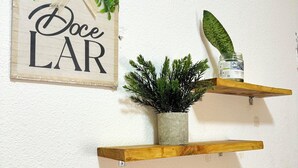 Een muur met drie houten planken, waarop elk een andere voorwerp staat: een plant in pot, een pot en een kaars.