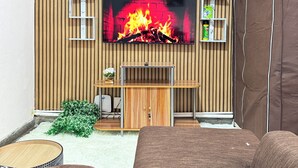 Een moderne woonkamer met een televisie bevestigd aan een houten wand, een kastje eronder en een bruine bank.