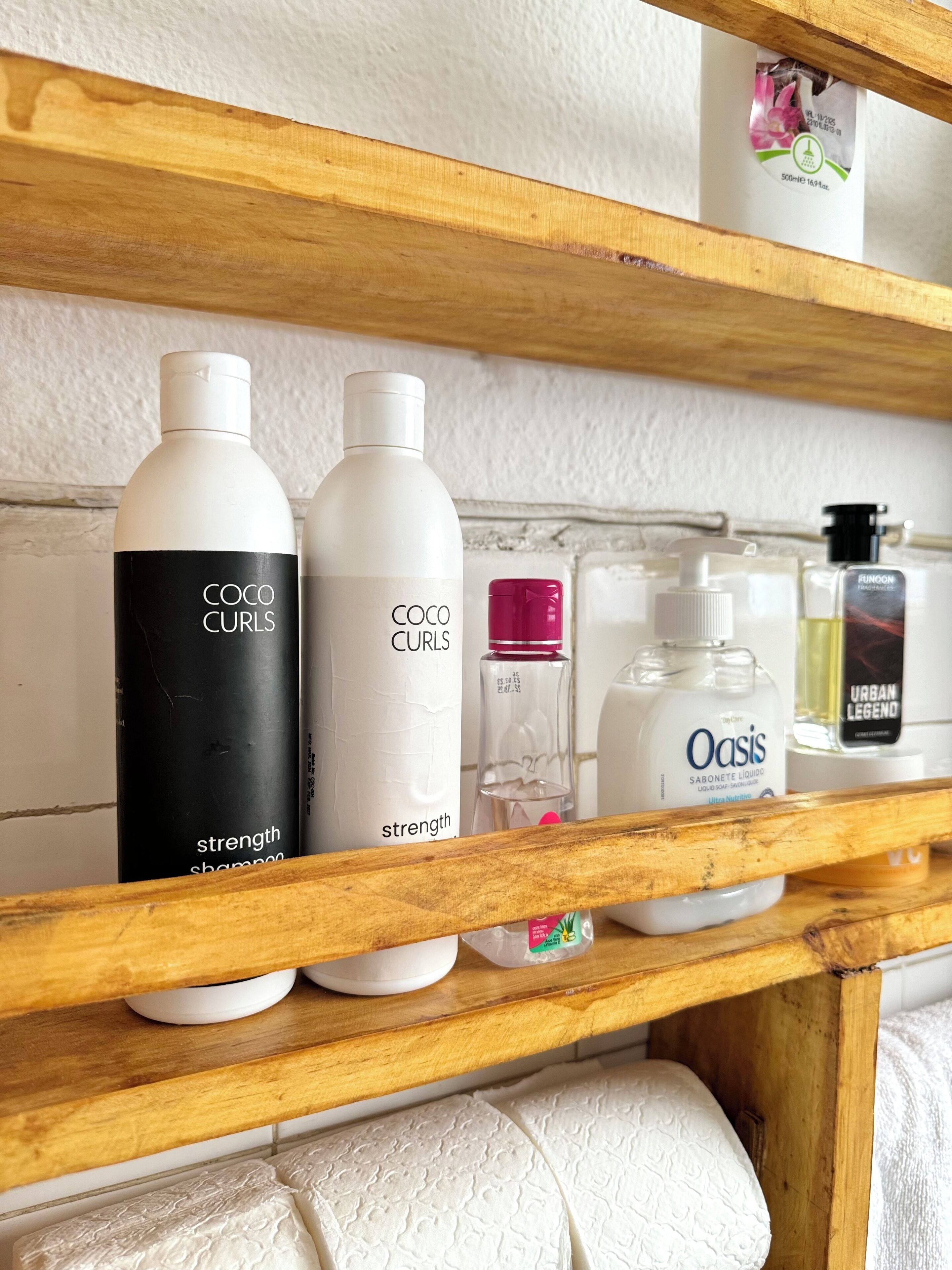 Une étagère contenant divers produits de toilette, notamment des flacons de shampoing Coco Curls, un flacon de savon Oasis et d’autres articles de soins personnels.