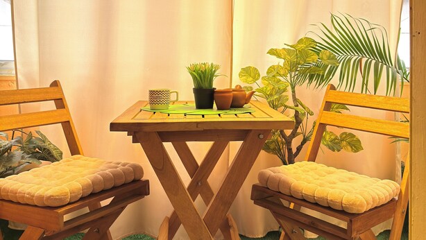 Een gezellig hoekje met een houten tafel en stoelen, een plant in pot en een hanglamp.