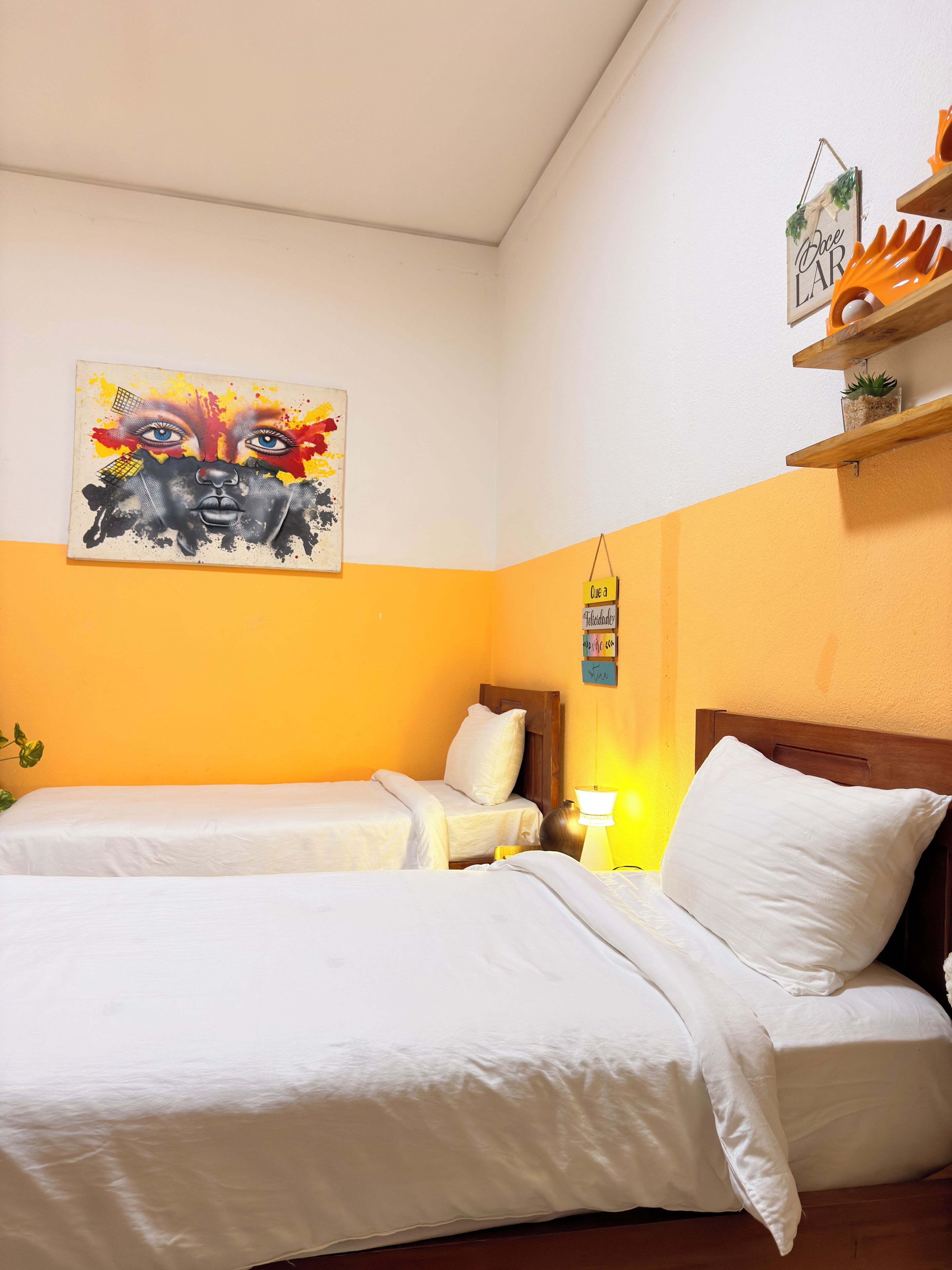 Una habitación de hotel con dos camas, un cuadro en la pared y un estante con objetos decorativos.