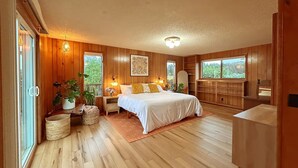 Une chambre avec des murs en bois, un lit, une télévision et une grande fenêtre.