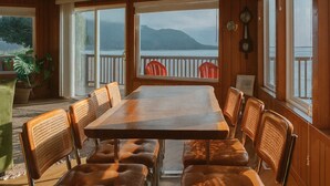 A wooden dining area with a large table and chairs, large windows with a view of mountains, and a ceiling fan. - Secluded, Bayfront Escape, Luxury Hot Tub, EV Charger, King Beds, Pets OK (Tillamook)