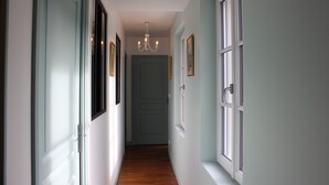 A hallway with white doors, a chandelier, and framed pictures on the walls.