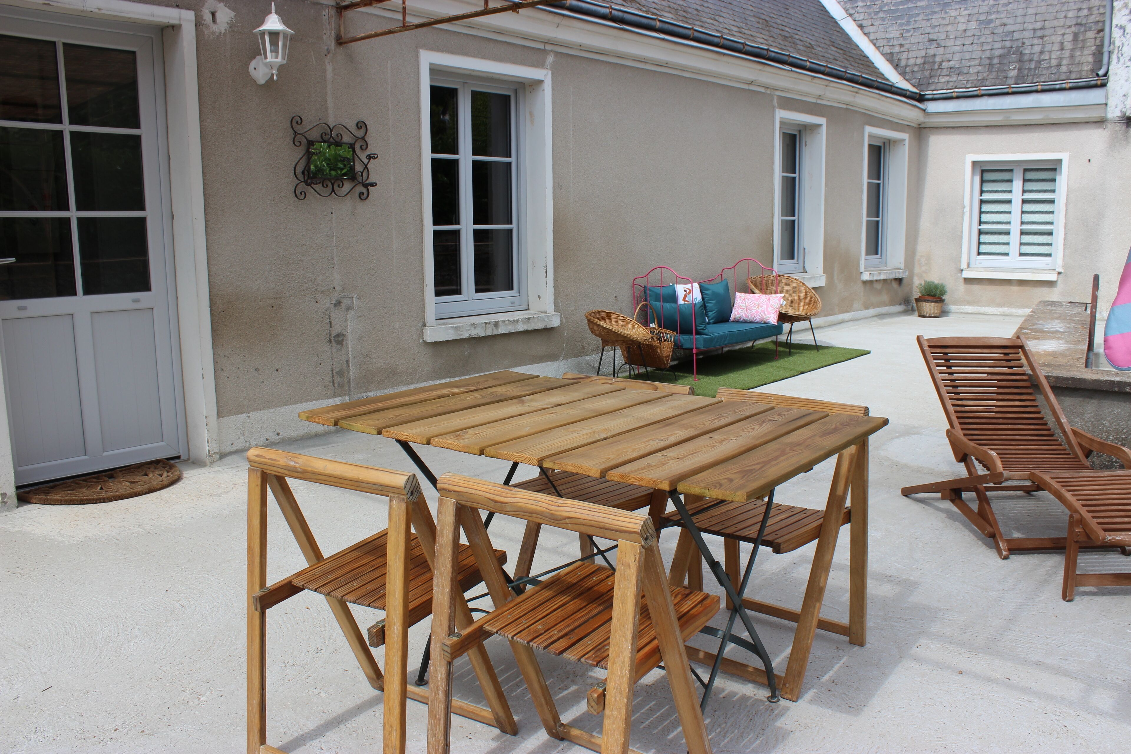 An outdoor patio with a wooden table and chairs, a wicker sofa, and a potted plant.