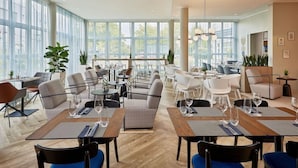 Un comedor moderno con varias mesas y sillas, ventanas amplias y plantas de interior.