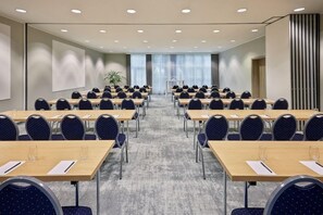 A conference room with rows of tables and chairs, a large screen, and a plant. - Courtyard by Marriott Dortmund (Dortmund)