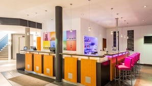Un área de recepción de hotel moderna con un mostrador central, varios taburetes de bar y una escalera al fondo.