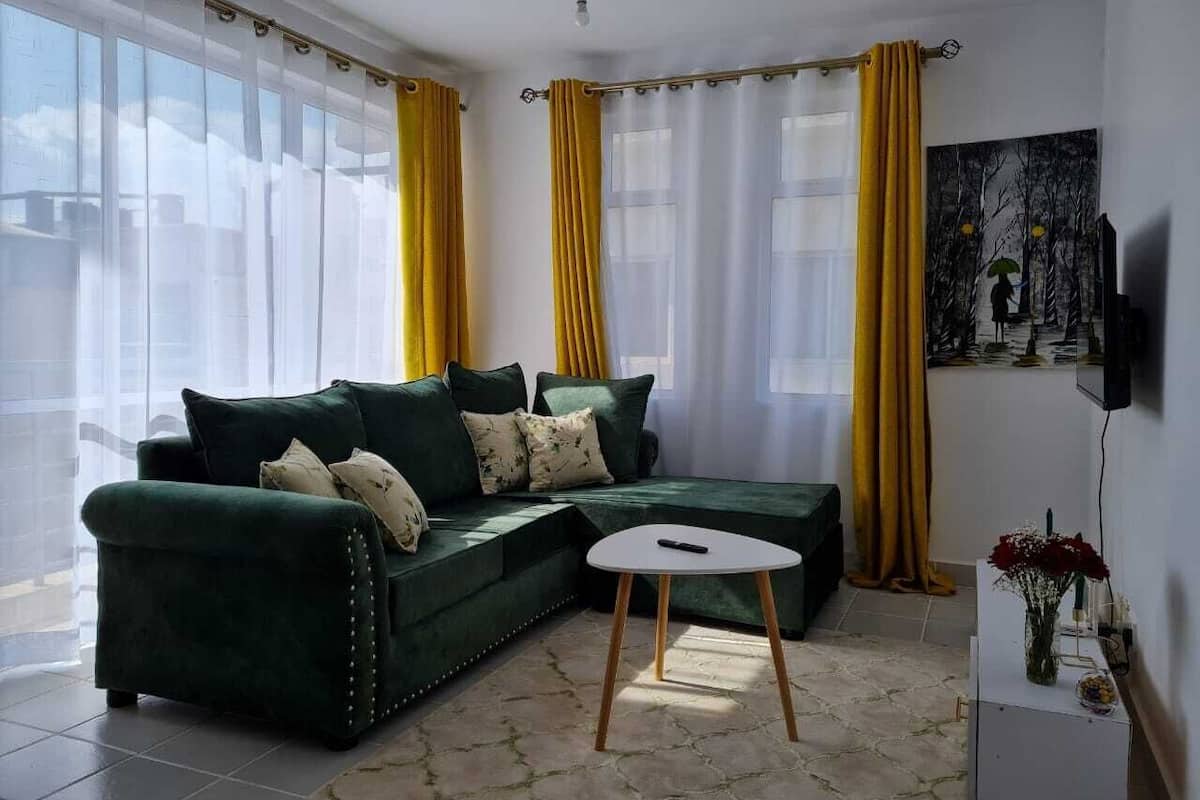 A living room with a green sofa, a small white table, and yellow curtains.