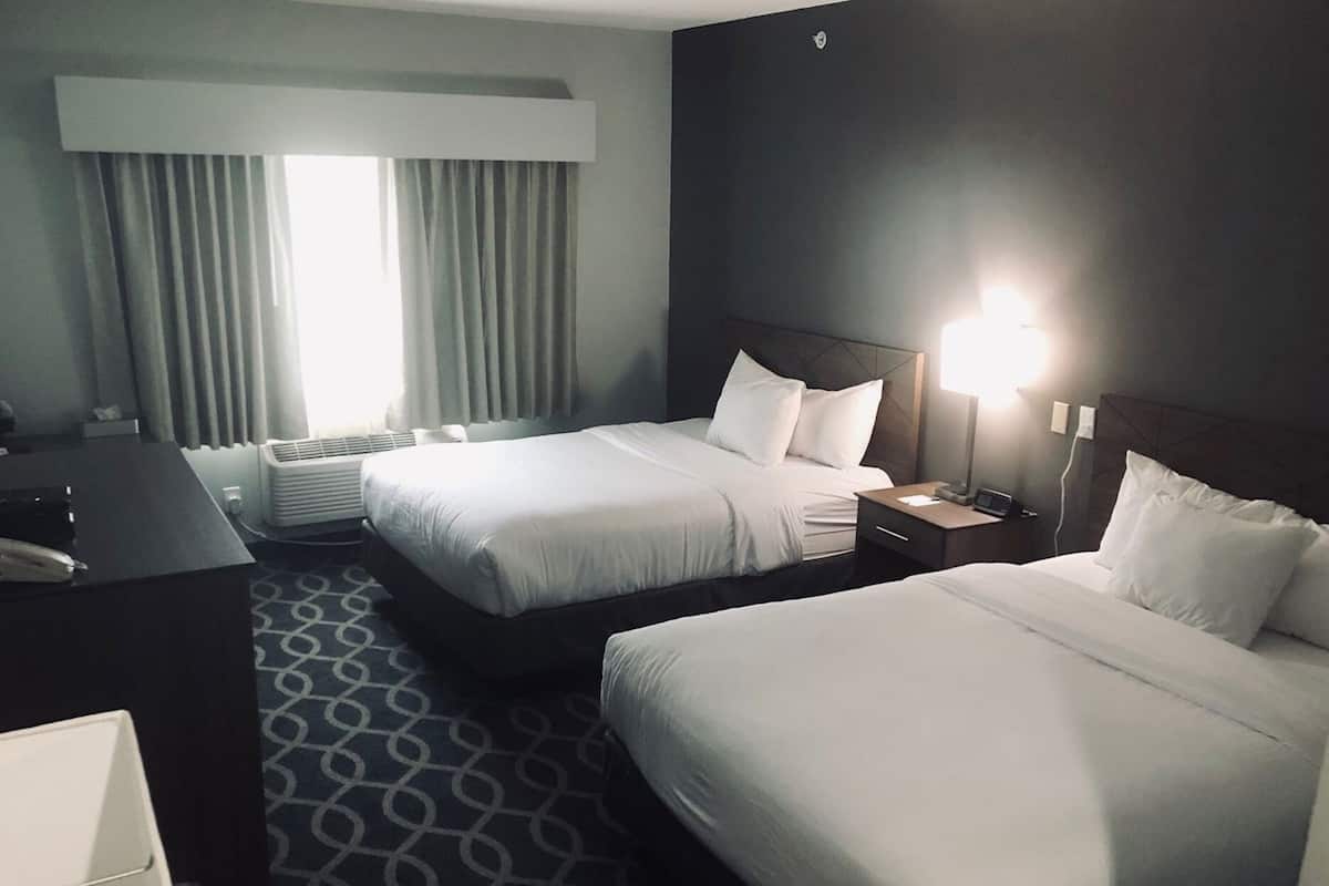 A hotel room with two beds, a desk, a chair, a lamp, and a window with curtains.