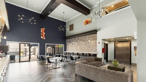 A modern hotel lobby with a herringbone wood floor, a sofa, and a dining area with tables and chairs. - Wingate by Wyndham Humble/houston Intercontinental Airport (Humble)