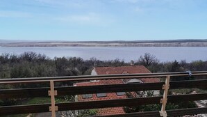 Blick vom Balkon auf einen See mit einer entfernten Uferlinie, umgeben von spärlicher Vegetation.