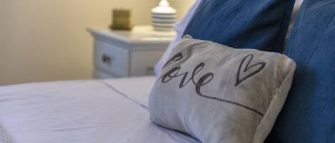 A neatly made bed with a pillow that has "love" and a heart symbol embroidered on it.