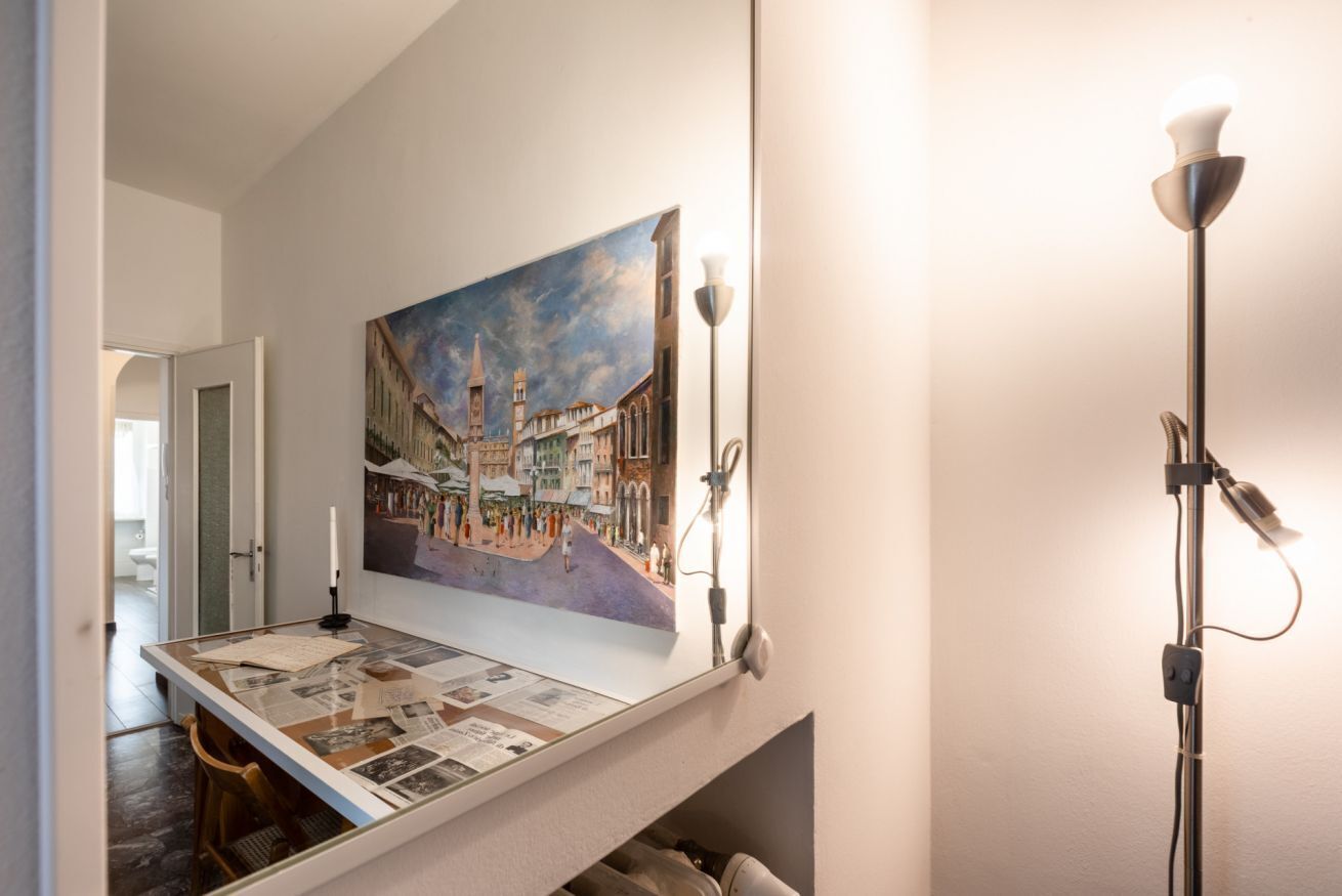 A room with a large painting of a cityscape, a table with papers, and a floor lamp.