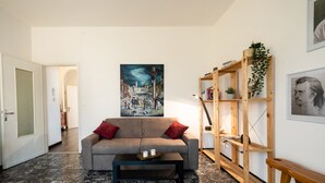 Una sala de estar con un sofá, una mesa de centro, una estantería de madera y un cuadro en la pared.