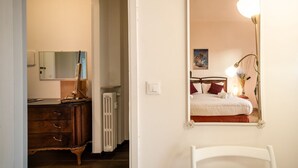 Un dormitorio con cama, lámpara de noche, cómoda y espejo en la pared.