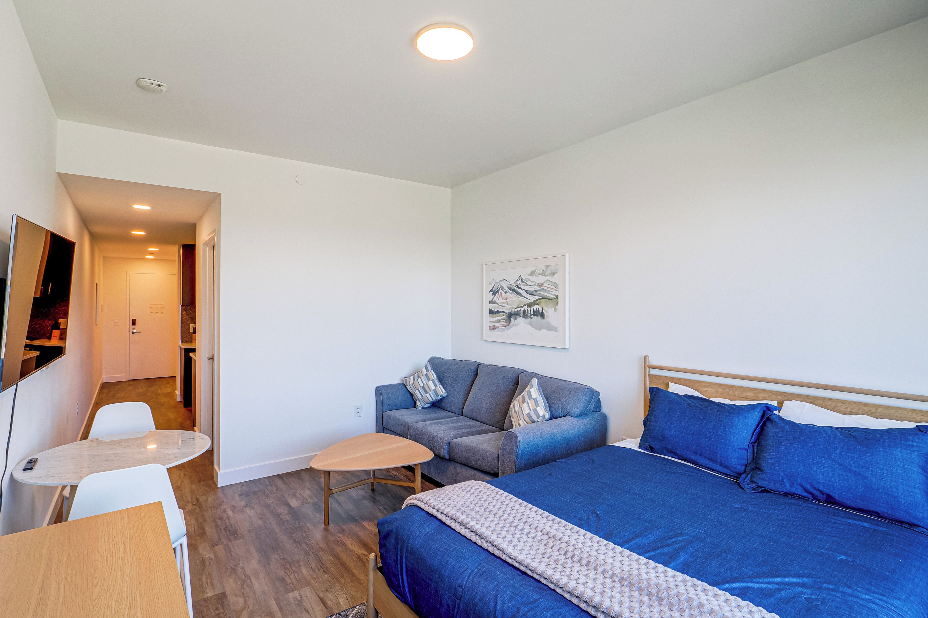 A modern hotel room with a bed, a sofa, a small table, and a desk.