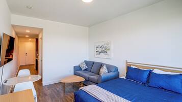 A modern hotel room with a bed, a sofa, a small table, and a desk.