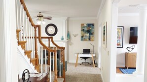A spacious hallway with a wooden staircase, a ceiling fan, a clock, and a desk with a chair. - Magnificent Villa To Unwind in a great location to Quantico (Fredericksburg)