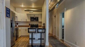 A modern kitchen with white cabinets, a microwave, a stove, and two bar stools. - Historic Haven Hideaway California King Bed

 (Cleveland)